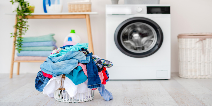 Heap of clothes for washing in basket standing on floor near washing machine in light bathroom