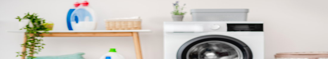 Heap of clothes for washing in basket standing on floor near washing machine in light bathroom