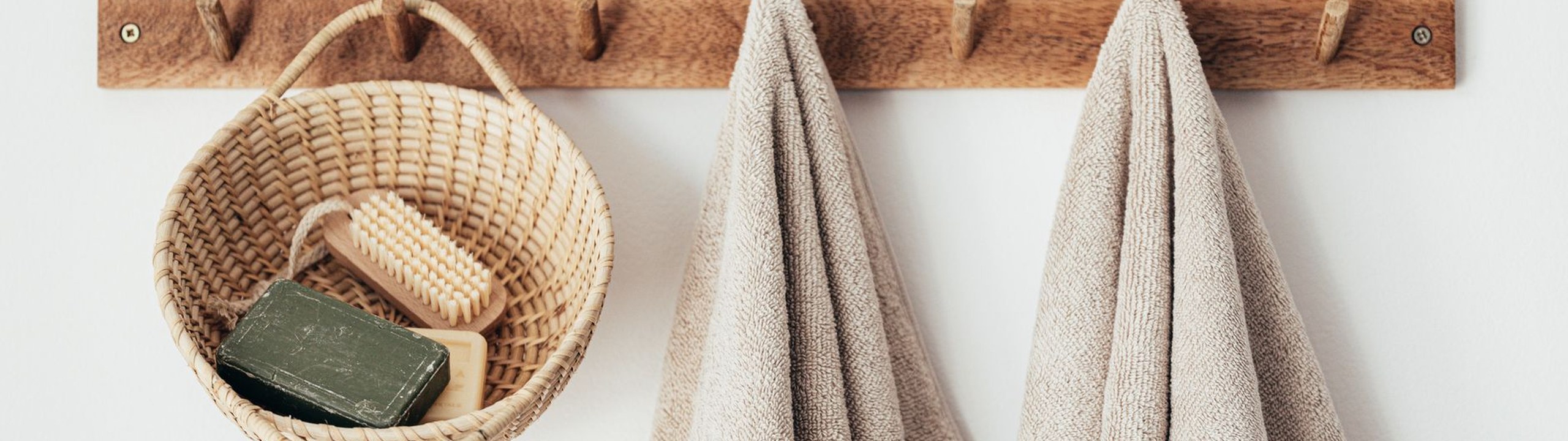 Neutral towels hanging on wooden wall hooks beside a basket of natural soap and a wooden brush