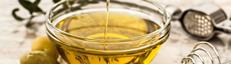 Olive oil being poured into a glass bowl with olives, a topic image for getting olive oil out of clothes